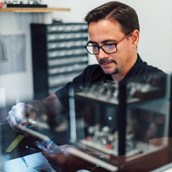 Urmakare med glasögon och handskar inspekterar noggrant ett armbandsur i en verkstad